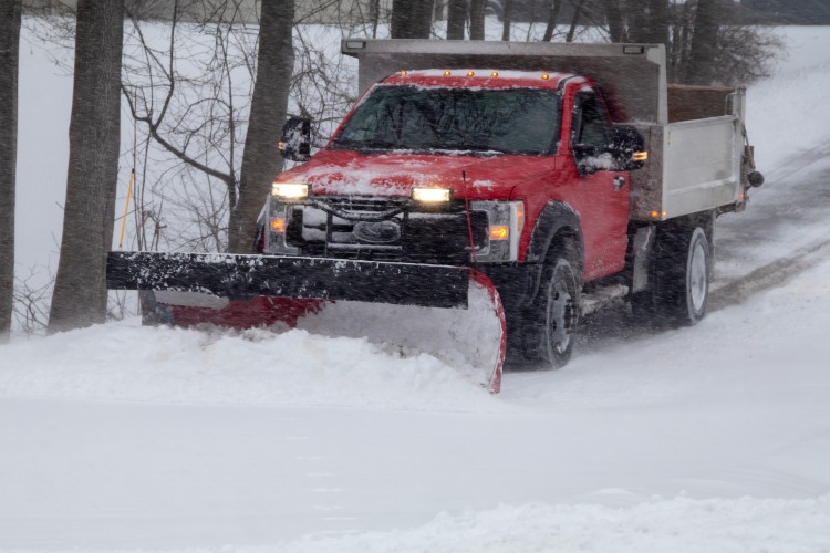 red truck with snow plow connected to the front plowing snow in a snow storm